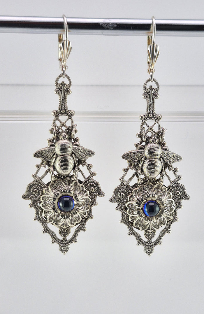 Sterling silver filled Victorian antique or reproduction work from original mold. The earrings feature an ornate silver filigree design embellished with a silver flower with iridescent royal blue mini cabochon  &  a silver bee motif, all mounted on lever back earring hooks.