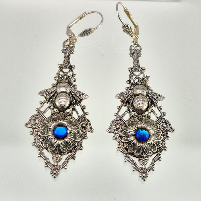 Sterling silver filled Victorian antique or reproduction work from original mold. The earrings feature an ornate silver filigree design embellished with a silver flower with iridescent royal blue mini cabochon  &  a silver bee motif, all mounted on lever back earring hooks.