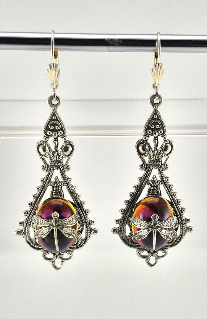 Sterling silver filled Victorian antique or reproduction work from original mold. The earrings feature an ornate silver filigree design surrounding a central purple & amber iridescent oval antique Art Glass cabochon with a dragonfly motif mounted on lever back earring hooks.
