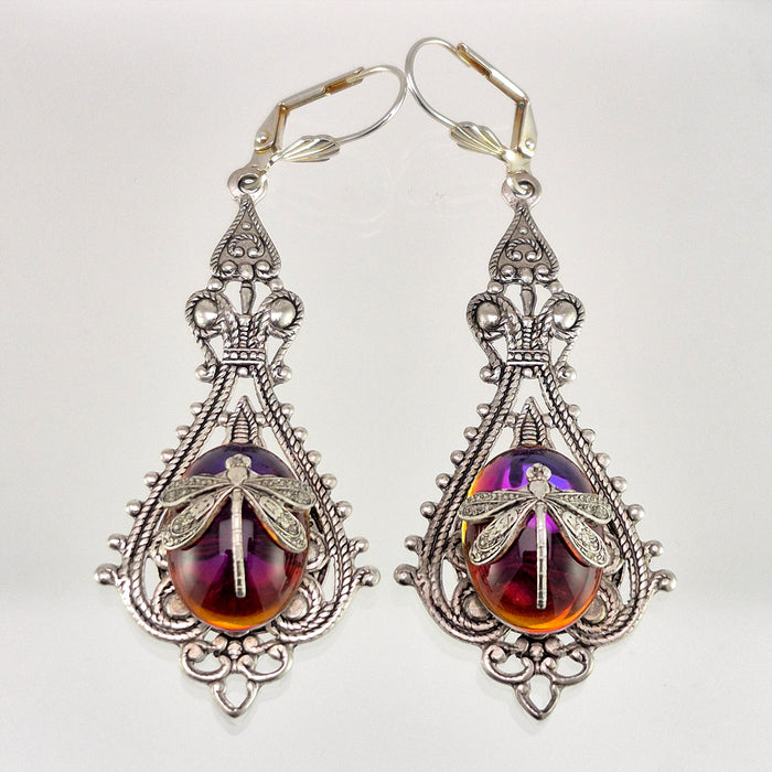 Sterling silver filled Victorian antique or reproduction work from original mold. The earrings feature an ornate silver filigree design surrounding a central purple & amber iridescent oval antique Art Glass cabochon with a dragonfly motif mounted on lever back earring hooks..