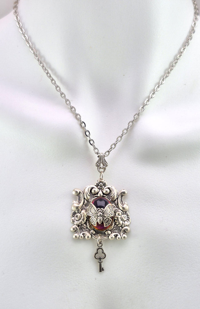 Sterling silver filled Victorian antique or reproduction work from original mold. The pendant features a silver floral design with silver key pendant surrounding a central purple & amber iridescent antique Art Glass cabochon with a butterfly motif.