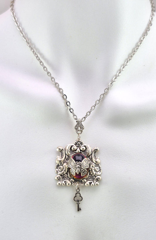 Sterling silver filled Victorian antique or reproduction work from original mold. The pendant features a silver floral design with silver key pendant surrounding a central purple & amber iridescent antique Art Glass cabochon with a butterfly motif.