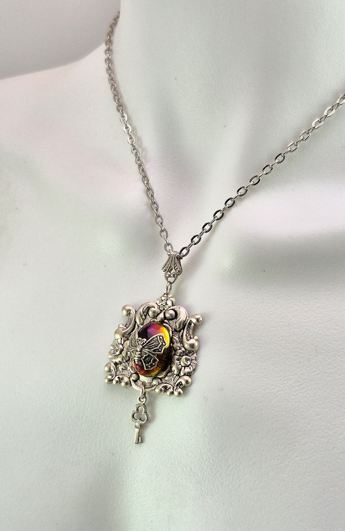 Sterling silver filled Victorian antique or reproduction work from original mold. The pendant features a silver floral design with silver key pendant surrounding a central purple & amber iridescent antique Art Glass cabochon with a butterfly motif.