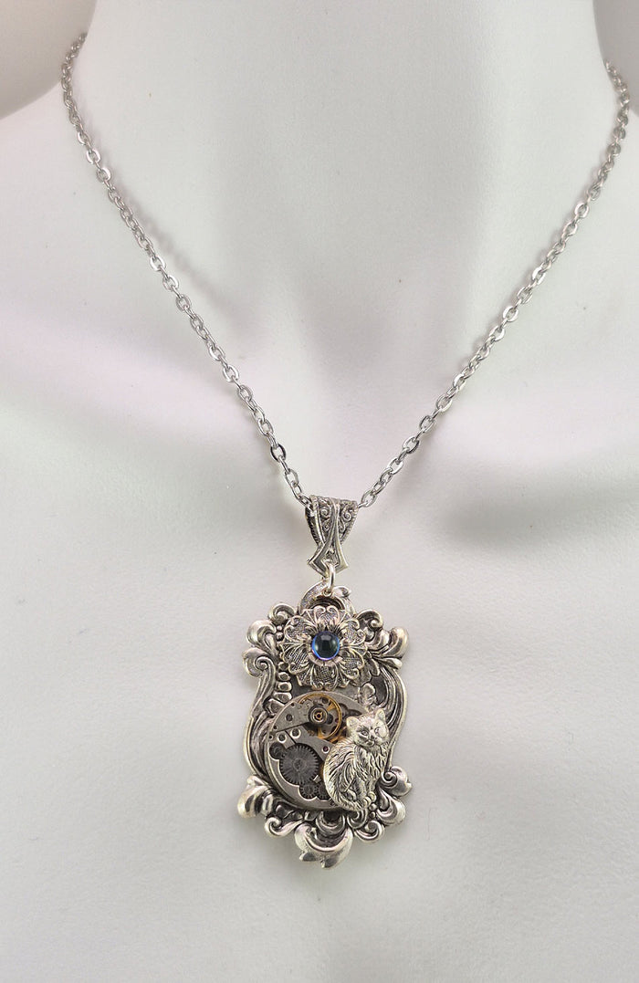Sterling silver filled Victorian antique or reproduction work from original mold. The pendant features an ornate silver floral design with mini cabochon surrounding a vintage clockworks embellished with a silver kitten.