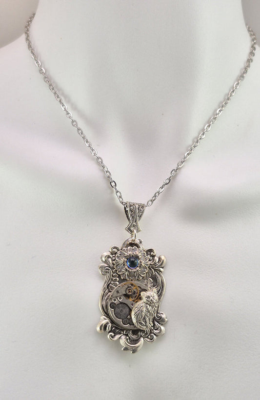 Sterling silver filled Victorian antique or reproduction work from original mold. The pendant features an ornate silver floral design with mini cabochon surrounding a vintage clockworks embellished with a silver kitten.