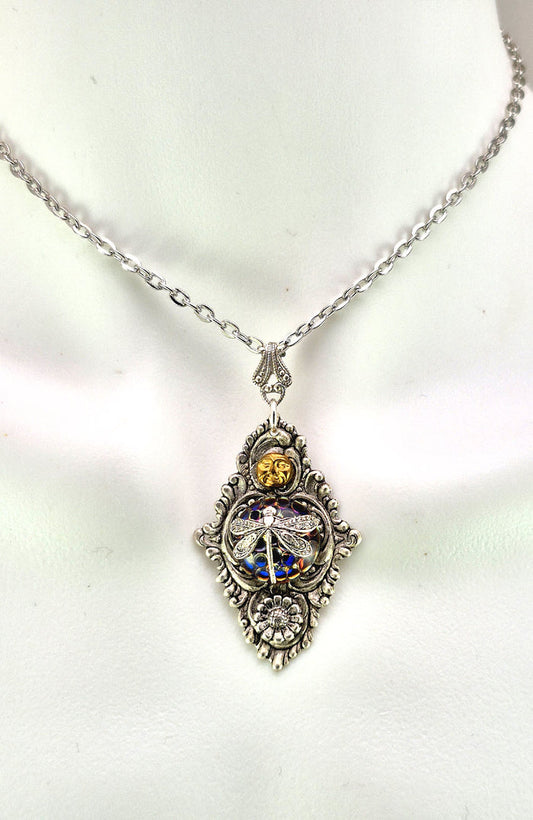 Sterling silver filled Victorian antique or reproduction work from original mold. The pendant features an ornate silver filigree design with brass moon and silver daisy surrounding a central blue & purple iridescent round antique Art Glass cabochon with a dragonfly motif.