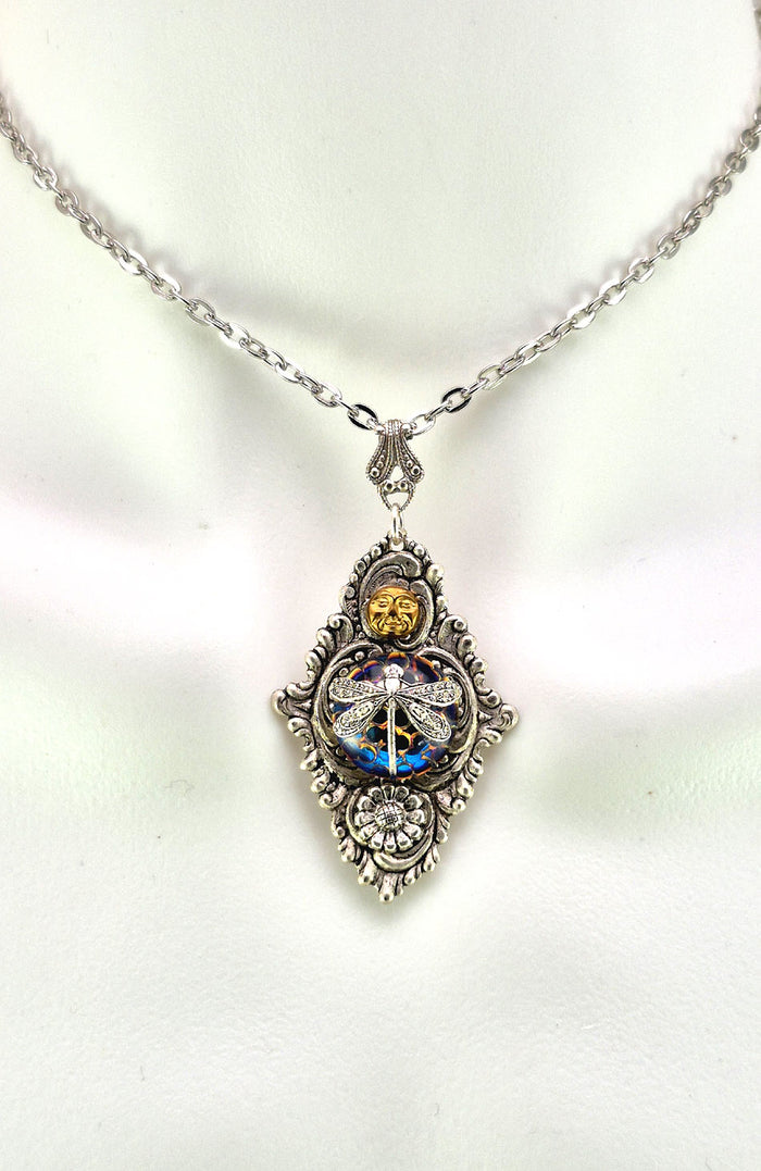 Sterling silver filled Victorian antique or reproduction work from original mold. The pendant features an ornate silver filigree design with brass moon and silver daisy surrounding a central blue iridescent round antique Art Glass cabochon with a dragonfly motif.