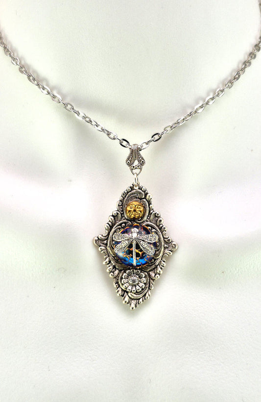 Sterling silver filled Victorian antique or reproduction work from original mold. The pendant features an ornate silver filigree design with brass moon and silver daisy surrounding a central blue iridescent round antique Art Glass cabochon with a dragonfly motif.