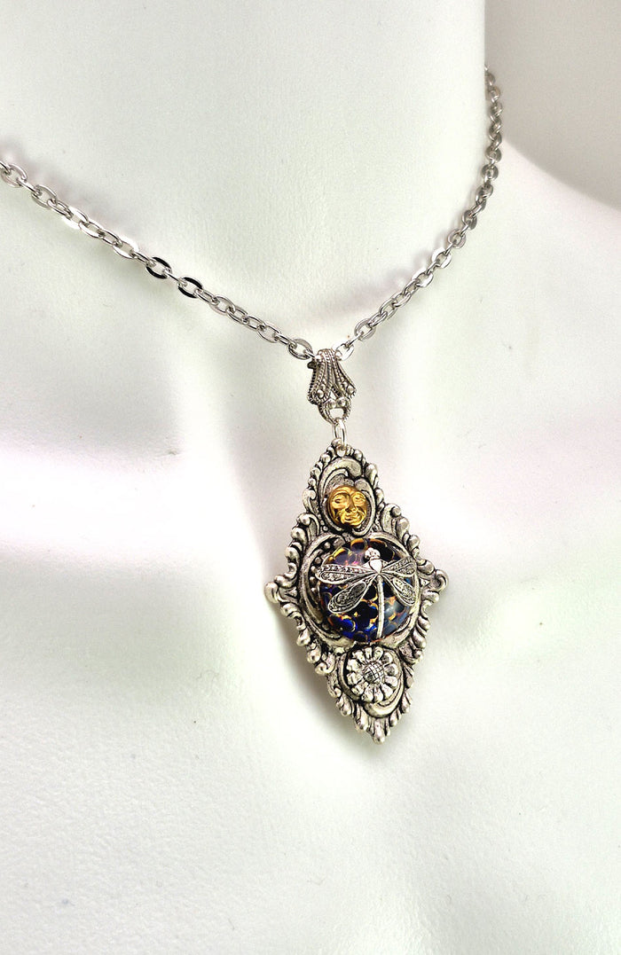 Sterling silver filled Victorian antique or reproduction work from original mold. The pendant features an ornate silver filigree design with brass moon and silver daisy surrounding a central blue iridescent round antique Art Glass cabochon with a dragonfly motif.