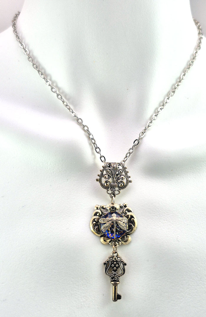 Sterling silver filled Victorian antique or reproduction work from original mold. The pendant features an simple baroque  design with silver key pendant surrounding a central blue & purple iridescent round antique Art Glass cabochon with a dragonfly motif.