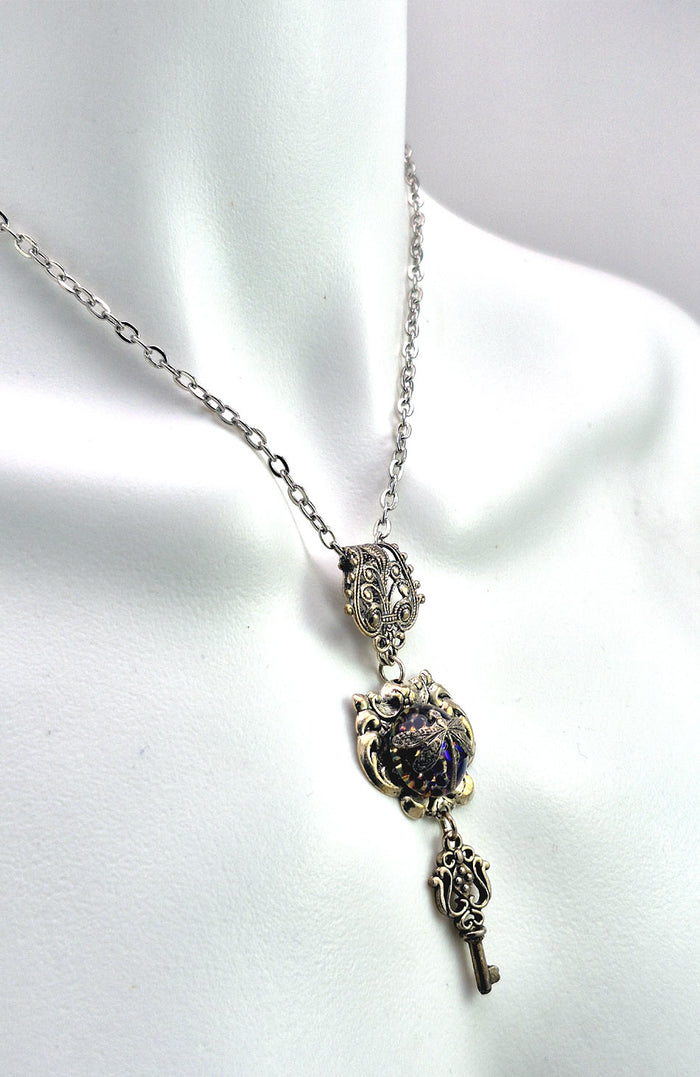 Sterling silver filled Victorian antique or reproduction work from original mold. The pendant features an simple baroque  design with silver key pendant surrounding a central blue & purple iridescent round antique Art Glass cabochon with a dragonfly motif.