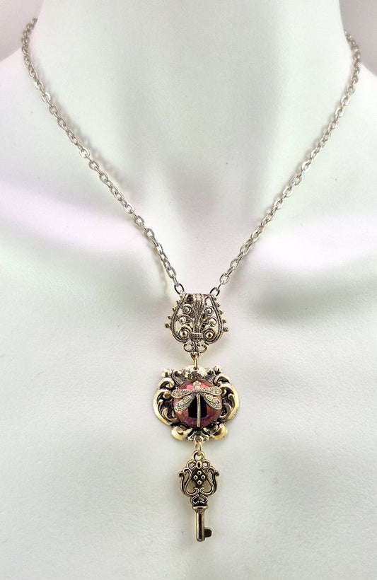 Sterling silver filled Victorian antique or reproduction work from original mold. The pendant features an simple baroque  design with silver key pendant surrounding a central lavender iridescent round antique Art Glass cabochon with a dragonfly motif.