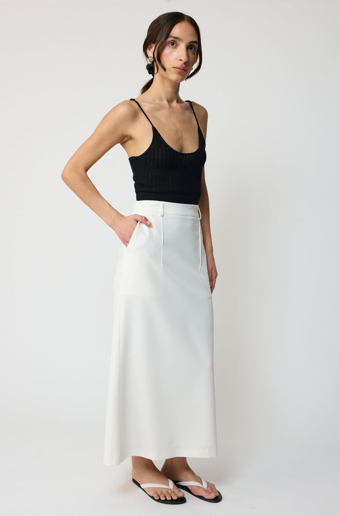 Woman wearing a black top and white skirt on a plain background