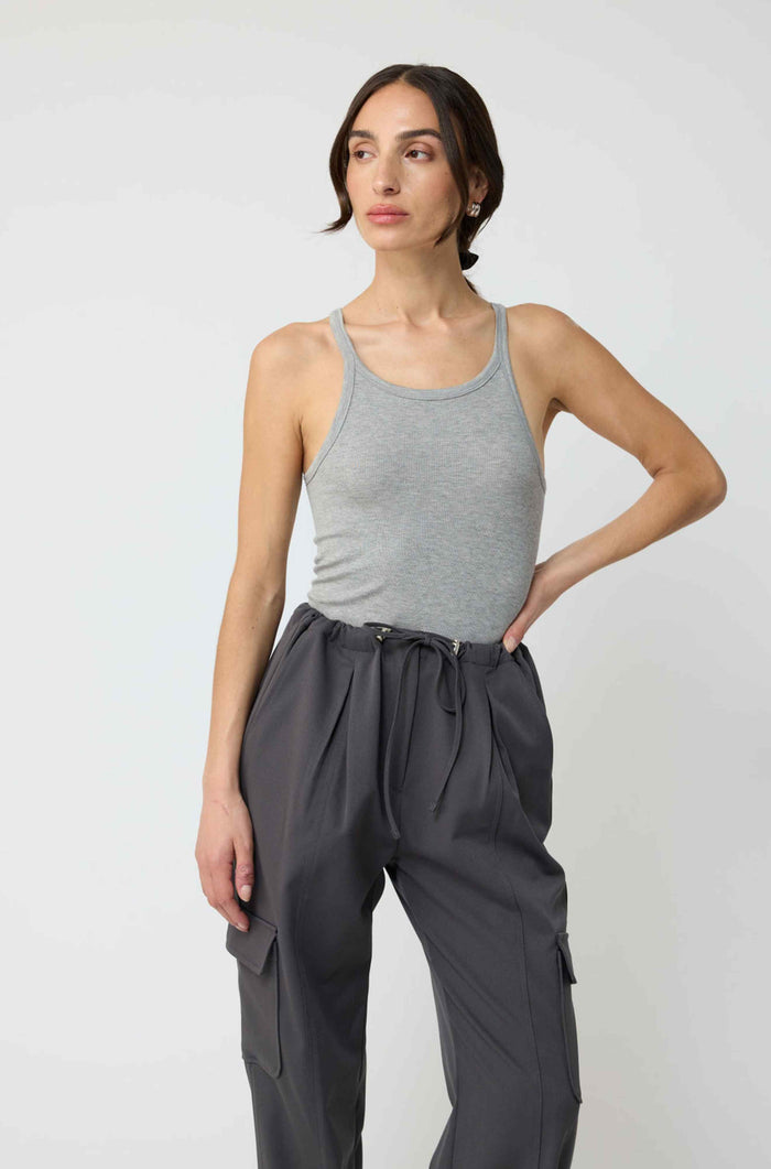 Woman wearing a gray tank top and dark gray pants against a white background