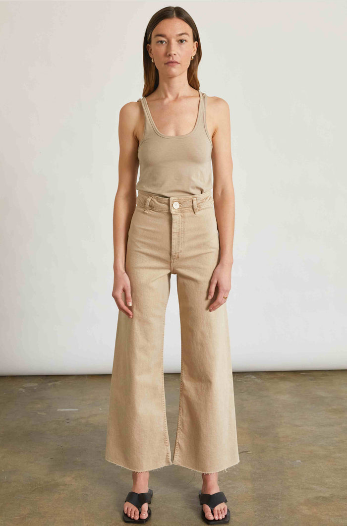 Woman wearing a beige tank top and wide-leg pants against a plain background