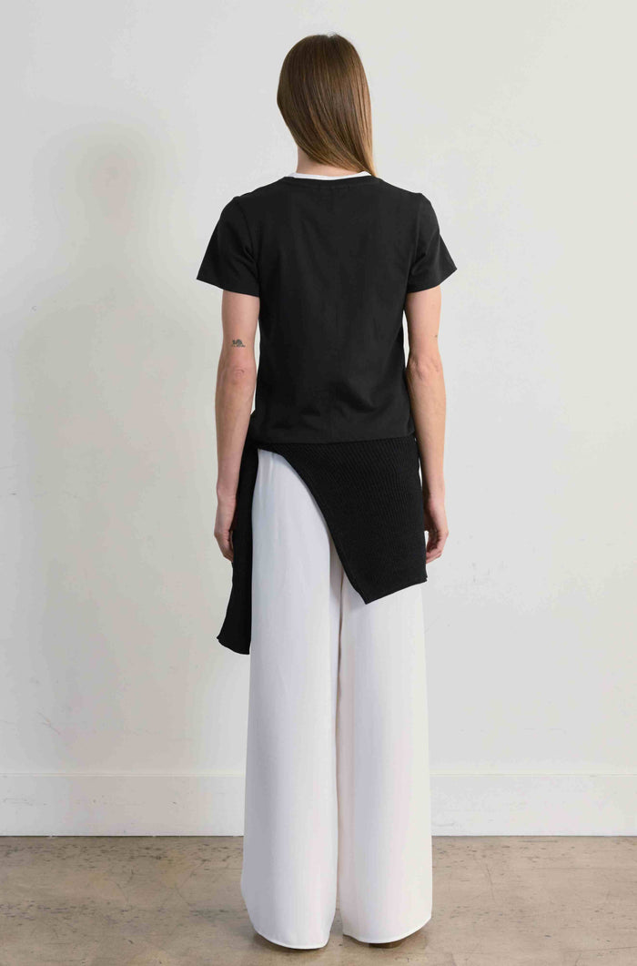 Person wearing a black top and white pants against a plain background