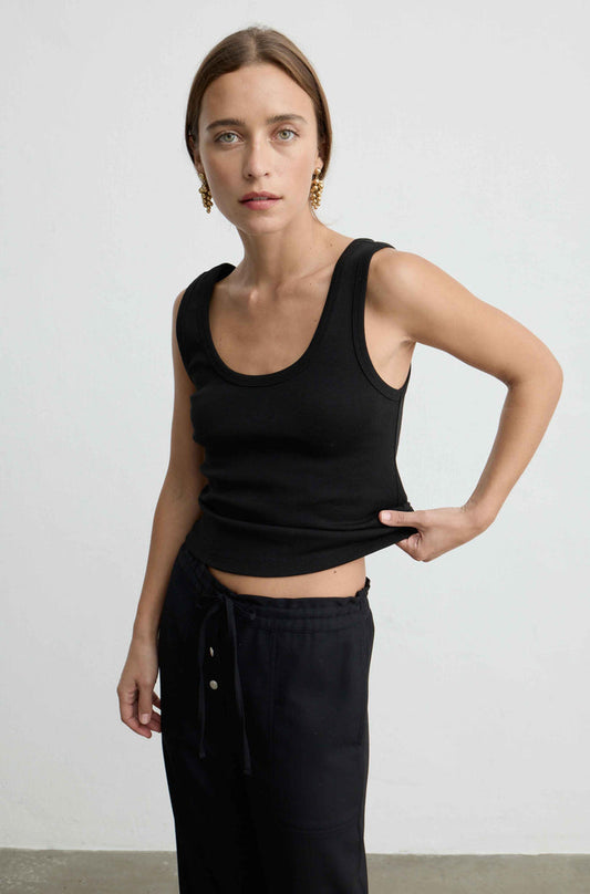 A woman modeling a black ribbed scoop-neck tank top and black drawstring pants against a plain light gray studio background.