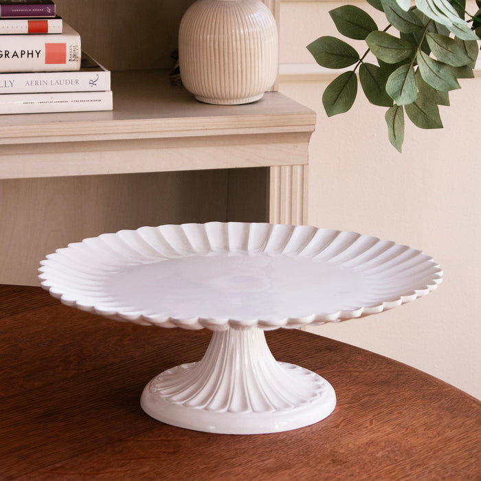 Beatriz Ball Vida Vienna Pedestal Cake Plate White — Empty stand beside books and a vase